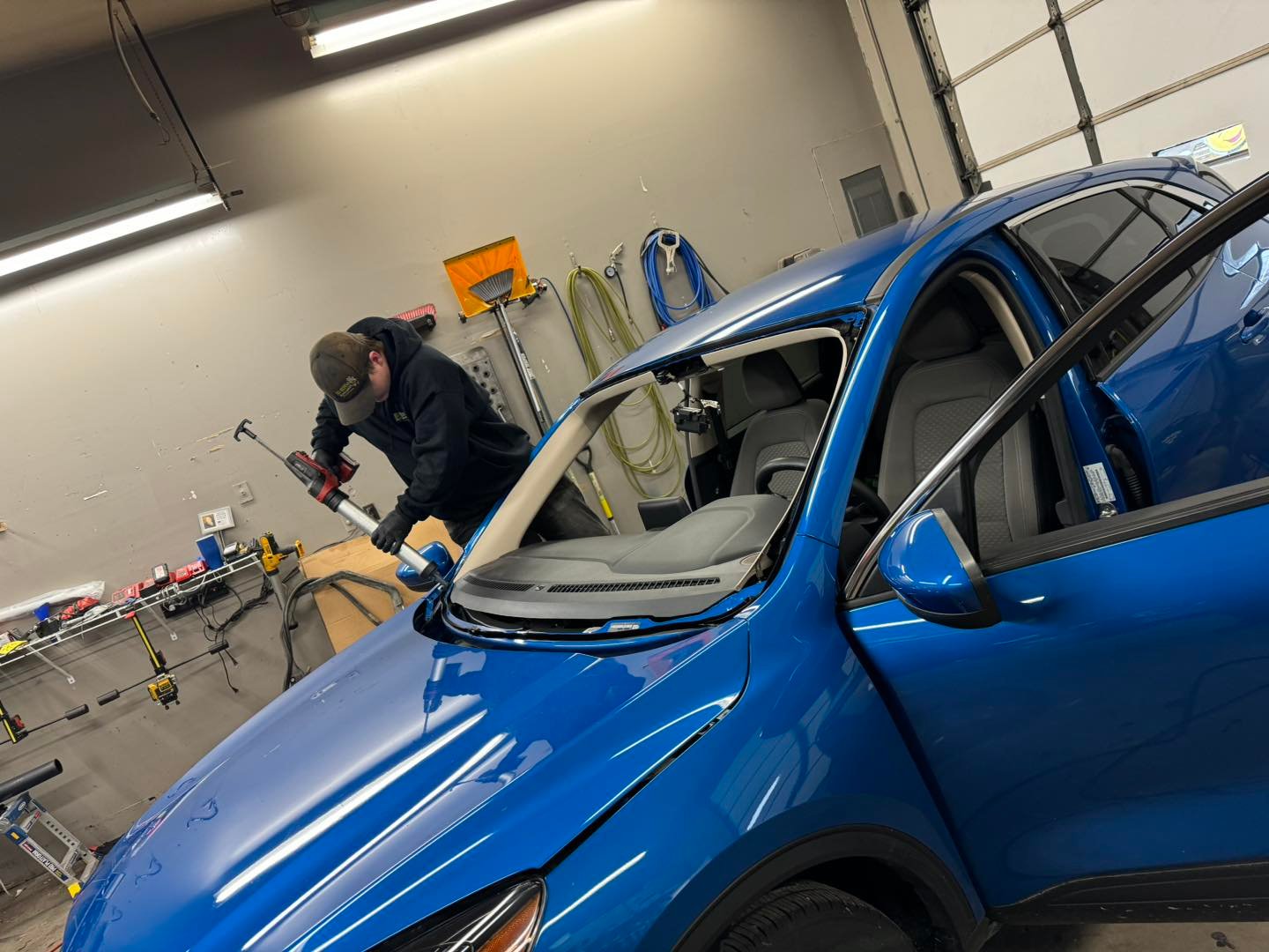Technician applying urethane sealant during windshield replacement on a blue SUV